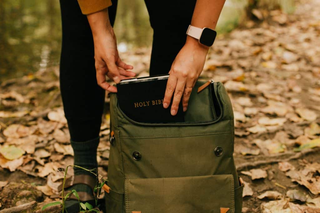 Bible verses about camping backpack Bible verses about camping image. Person putting a Bible into a backpack in the woods.