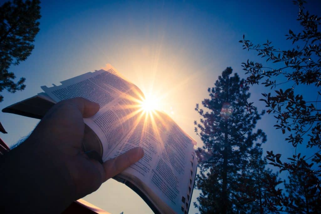 Bible verses about camping sunset bible verses about camping with hand lifting Bible to the sunset